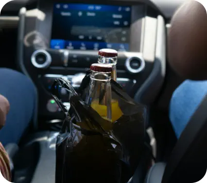 Two bottles of beer sit in a bag on the console of a car between the driver and passenger seats