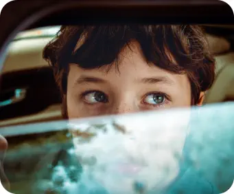 A young boy looks worriedly out of a car window