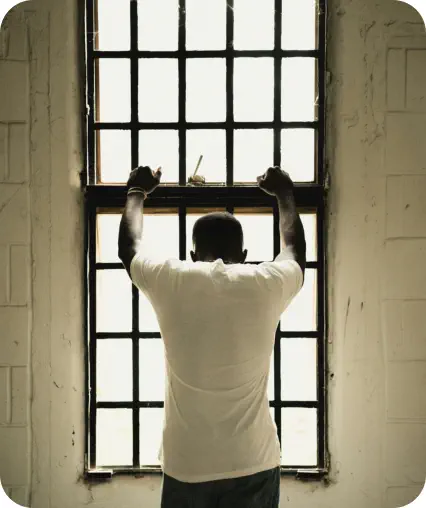 A young man faces away from the camera, leaning on a window frame an looking out of the window