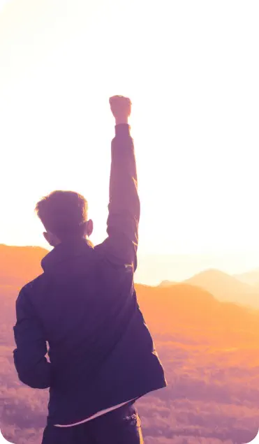 Young man wiht short hair looking at the sunrise and holding his fist in the air in a gesture of victory