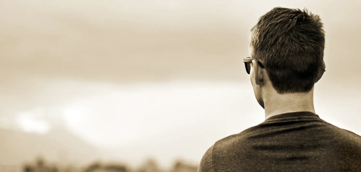 Background image of man with short hair and sunglasses facing away from the camera and staring at the horizon