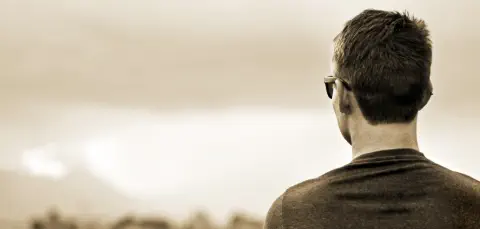 Background image of man with short hair and sunglasses facing away from the camera and staring at the horizon