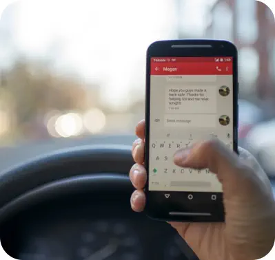 Closeup of a hand holding a mobile phone and texting while driving