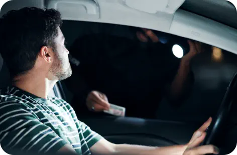 A young male driver at a traffic stop with his window down talking to a police officer who is holding his drivers license