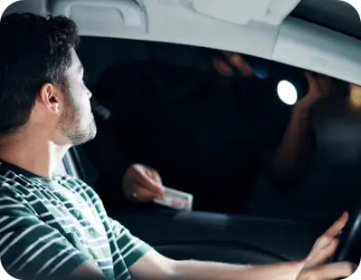 A young male driver at a traffic stop with his window down talking to a police officer who is holding his drivers license