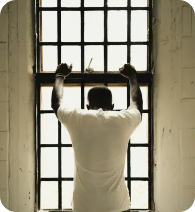 A young man faces away from the camera, leaning on a window frame an looking out of the window